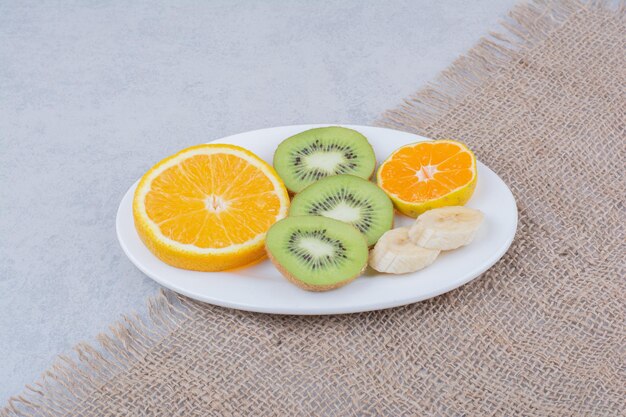 A white plate of sliced fruits on sackcloth. High quality photo