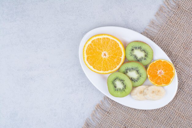 A white plate of sliced fruits on sackcloth.