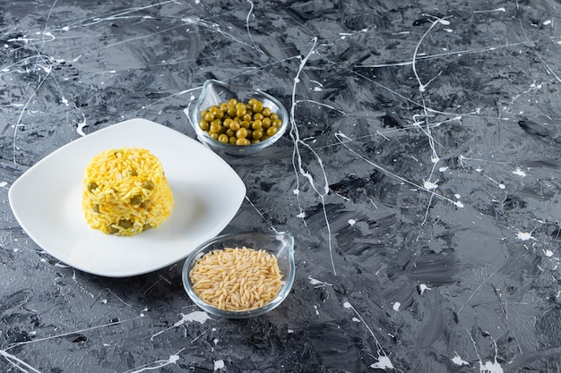 White plate of steamed rice with green peas on marble background. 