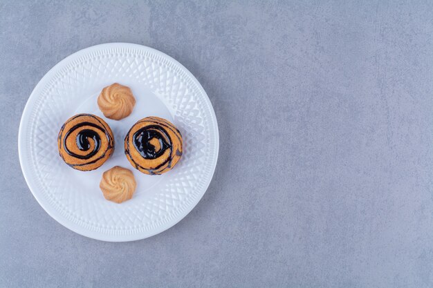 A white plate of sweet delicious cookies with chocolate syrup. 