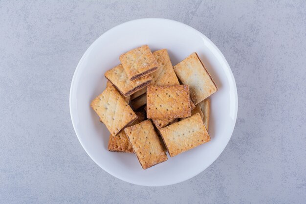 White plate of tasty crunchy crackers on stone table. 