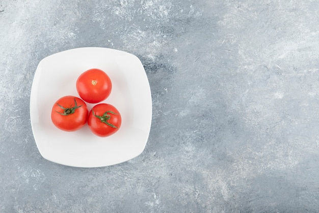 Foto gratuita un piatto bianco di tre pomodori rossi freschi su una priorità bassa di pietra.