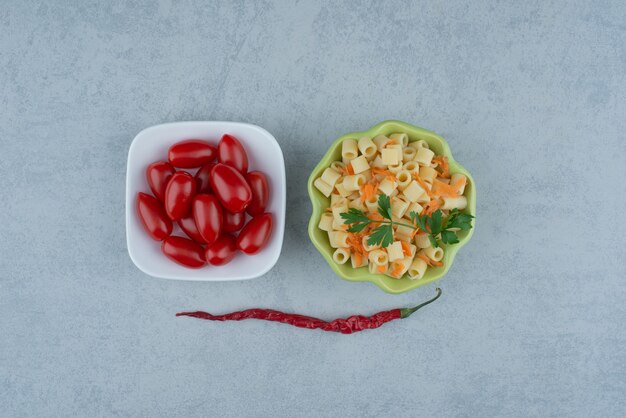 White plate of tomato cherry and green plate of delicious macaroni . High quality photo