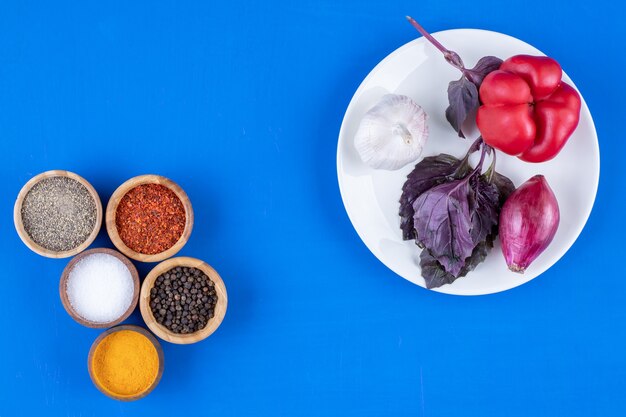 White plate of tomato, garlic and onion on blue surface. 