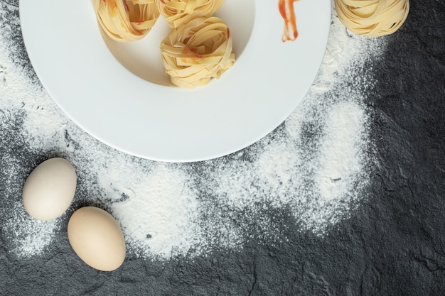 A white plate of uncooked nest noodles with red pepper.