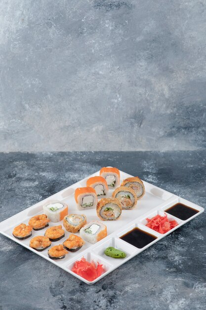 White plate of various delicious sushi rolls on marble background