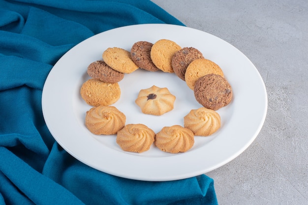 White plate of various sweet biscuits on stone table.