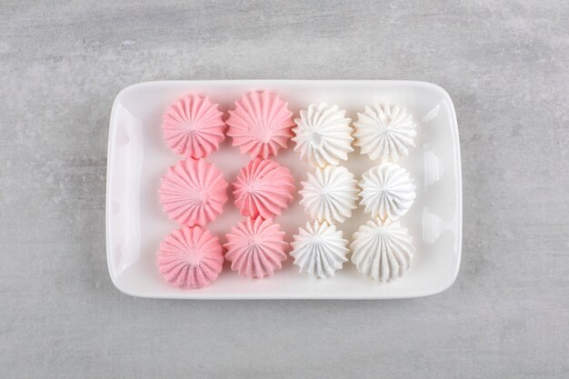 White plate of white and pink meringue sweets on stone table. 