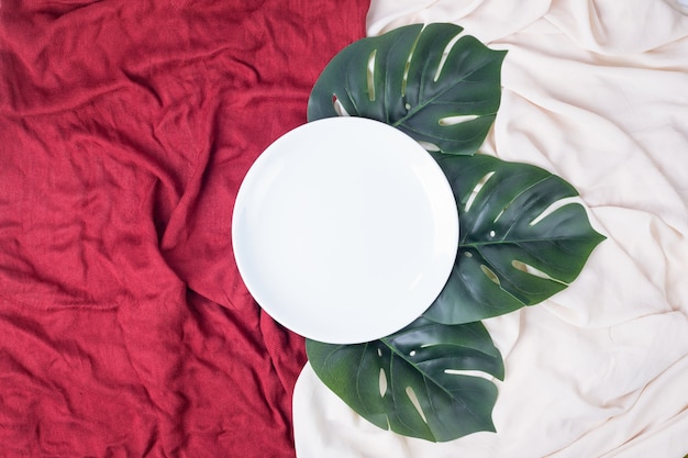 Белая тарелка с искусственными листьями на скатертях.