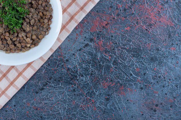 A white plate with beans and herbs on a tablecloth.