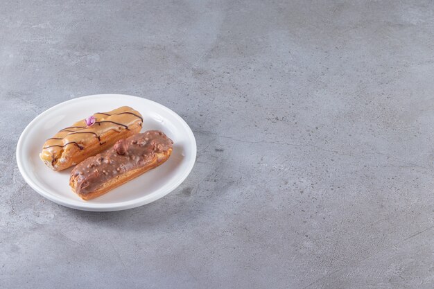 White plate with caramel and chocolate eclairs on stone surface