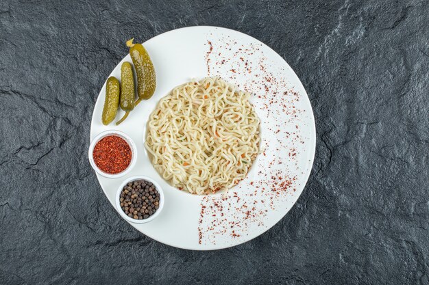 A white plate with delicious noodles and pickled gherkins. 