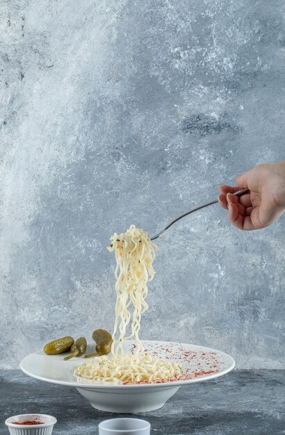 Un piatto bianco con deliziose tagliatelle e cetriolini sottaceto.