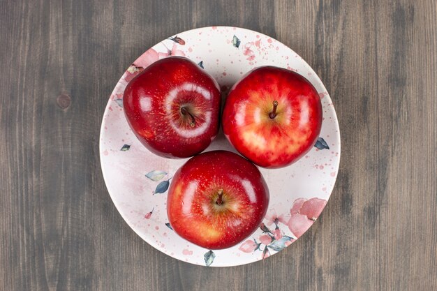 A white plate with red juicy apples on a wooden table. High quality photo