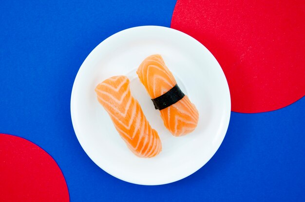 White plate with salmon sushi on a blue and red background