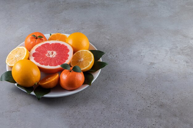 大理石のテーブルにスライスしたオレンジ、オレンジ、グレープフルーツの白いプレート。