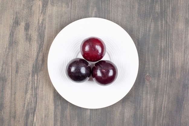 A white plate with three fresh plums on a wooden table. High quality photo