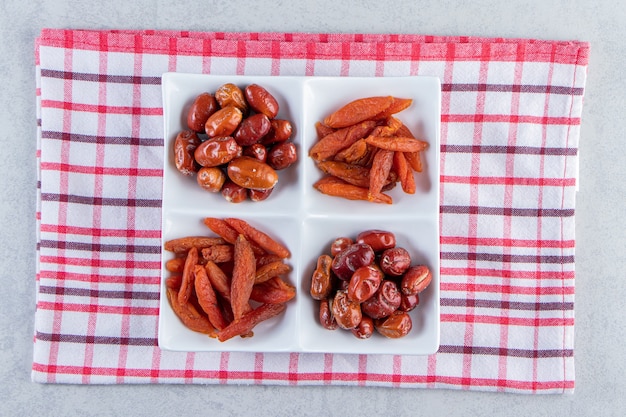 Piatto bianco con vari deliziosi frutti secchi su pietra.