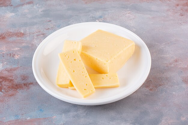White plate of yellow cheese slices on marble surface.