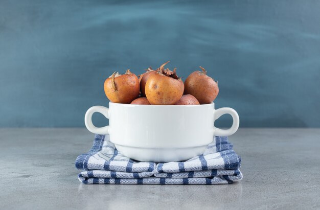 A white pot with fresh persimmons on a tablecloth . High quality photo