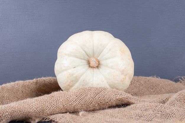 Free photo white pumpkin on blue surface with burlap.