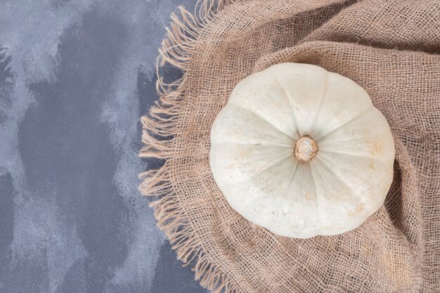 White pumpkin on blue surface with burlap.