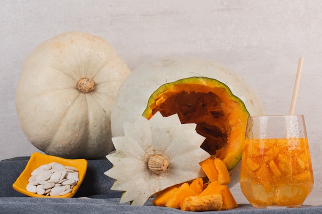 Free photo white pumpkin, glass of juice and pumpkin seeds on blue tablecloth.