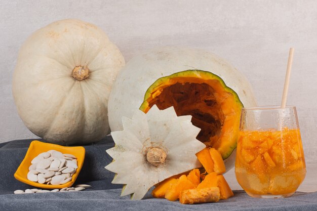 White pumpkin, glass of juice and pumpkin seeds on white table.