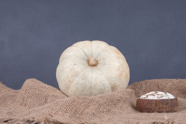 White pumpkin and seeds on blue surface with burlap.