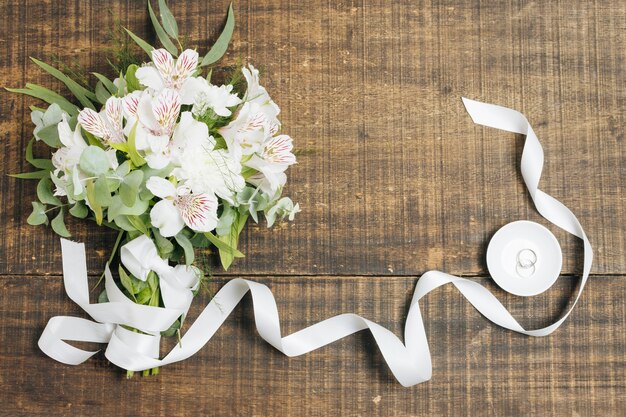 나무 책상 위에 접시에 결혼 반지와 화이트 리본 및 꽃 꽃다발