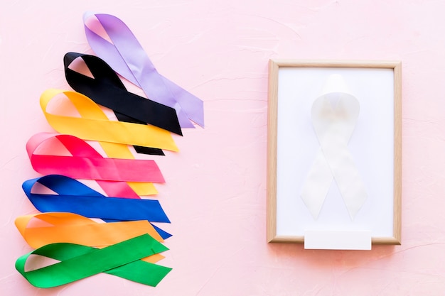 White ribbon on white wooden frame near the row of colorful awareness ribbon
