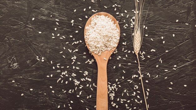 White rice grains on wooden spoon over rough gray background