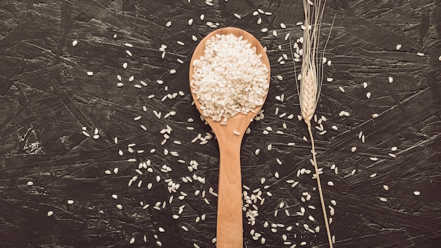 거친 회색 배경 위에 나무로되는 숟가락에 흰 쌀 곡물