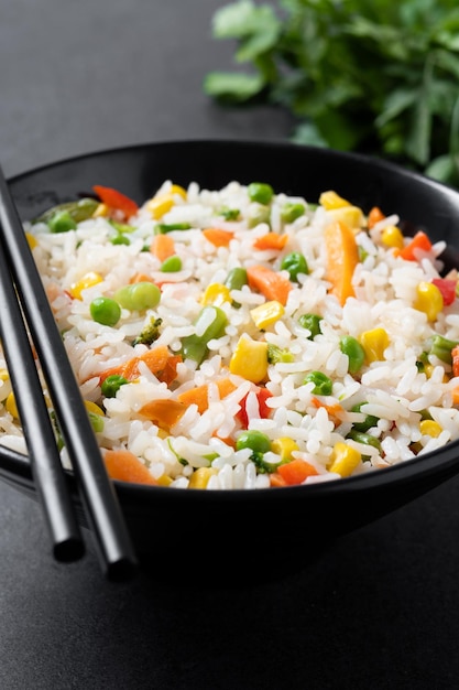 Free photo white rice with vegetables in a black bowl on black background
