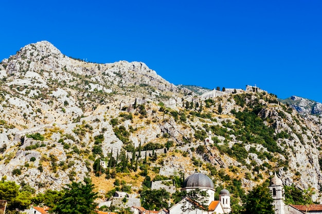 White rocky mountainside with green trees against a blue sky
