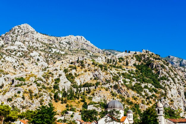 White rocky mountainside with green trees against a blue sky