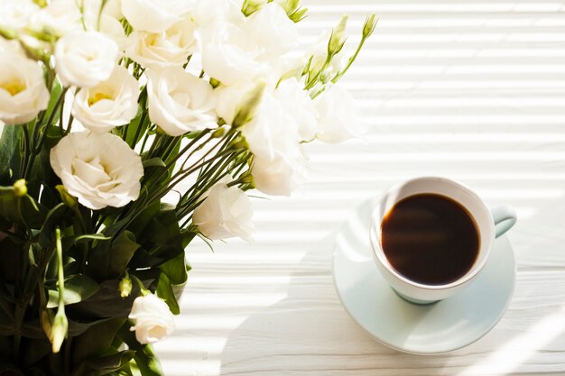 机の上のブラックコーヒーカップと白いバラの花束