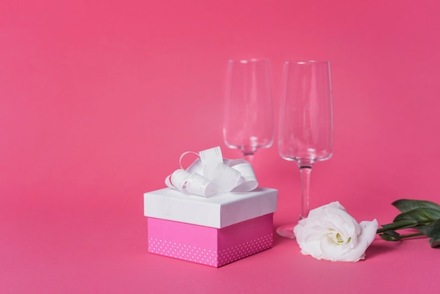 하얀 장미; 분홍색 배경에 선물 상자와 샴페인 플루트 안경