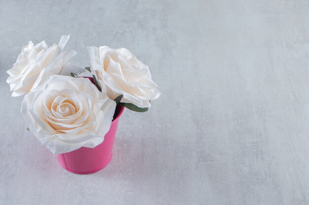 White roses in a pink bucket, on the white table.