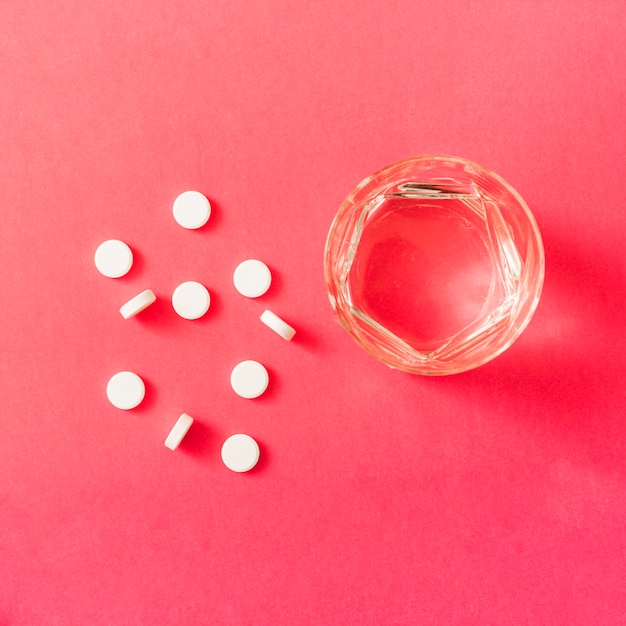 Белые круглые таблетки и стакан воды на красном фоне