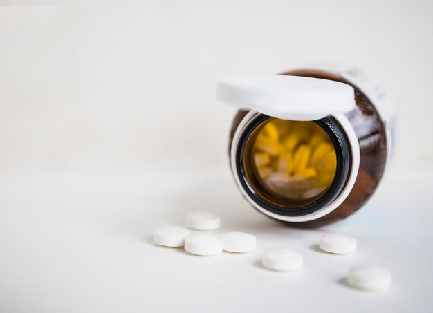 White round pills spilling from brown bottle on white background