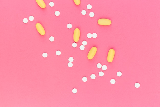 Белые круглые и желтые овальные таблетки на розовом фоне