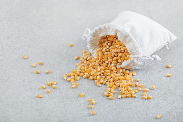 A white sack full of corn grains on a gray surface.