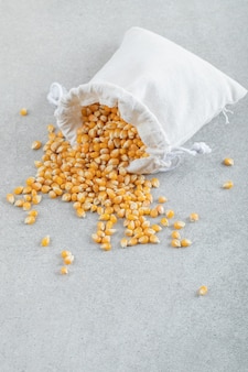 Un sacco bianco pieno di chicchi di mais su una superficie grigia.