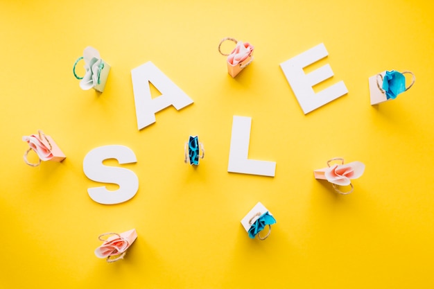 White sale alphabet surrounded with miniature shopping bags on yellow backdrop