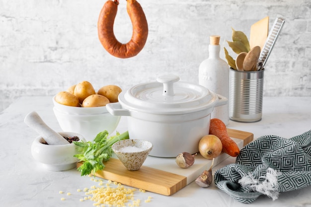 Free photo a white saucepan and ingredients for making minestrone soup with smoked sausage on a white table italian soup with pasta and seasonal vegetables