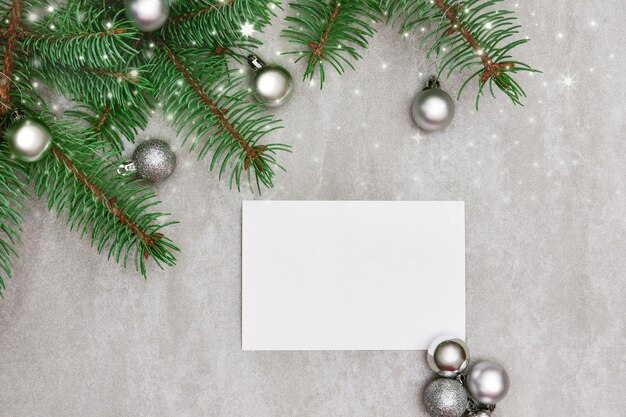 Белый лист бумаги на сером фоне с веточкой ели, праздничными шарами и серебряными огнями. Premium Фотографии