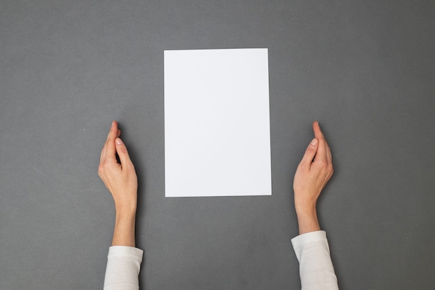 White sheet of paper for your text. woman holding an empty sheet of paper over gray texture. overhead view