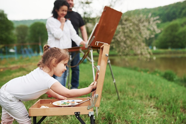 In white shirt. Grandmother and grandfather have fun outdoors with granddaughter. Painting conception
