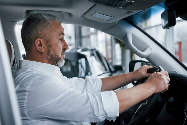 白いシャツとロールアップした袖。オートサロンで新しい高級車をしようとしている公式の服の上級ビジネスマン